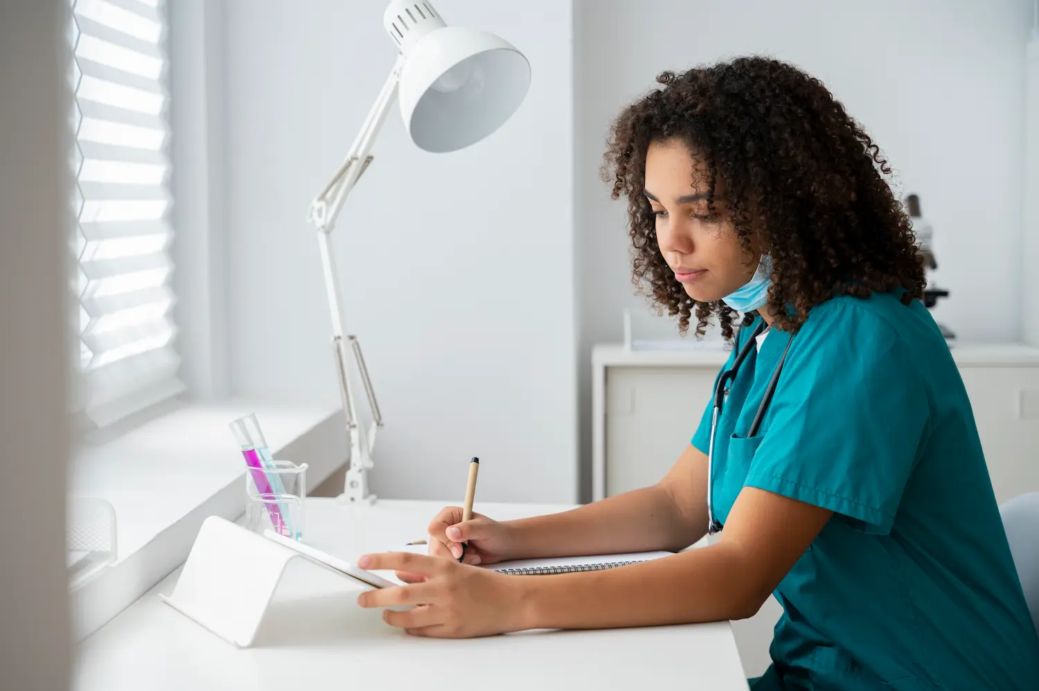 La verdad sobre la profesión del auxiliar de medicina estética 4 Chica estudiando un curso de auxiliar de medicina estética sobre un escritorio blanco con una tablet y un flexo